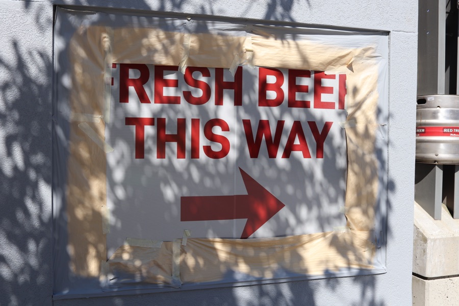 A makeshift sign taped into a wall recess reads FRESH BEER THIS WAY in red capitals above a right-pointing arrow.