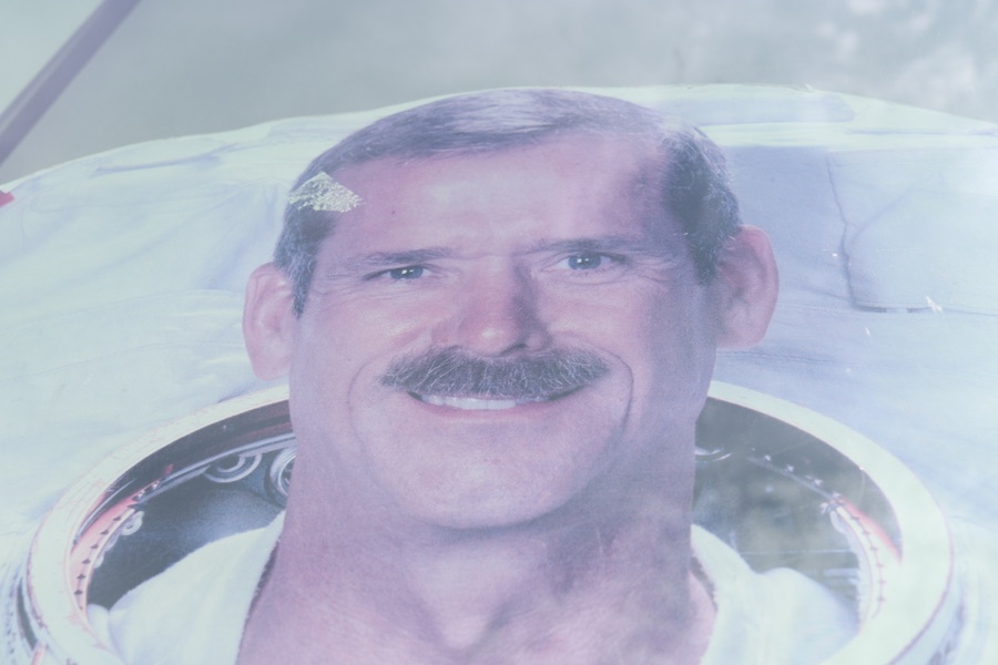A faded pink-and-blue printed portrait of a smiling moustached astronaut, closely framed behind a reflective surface.